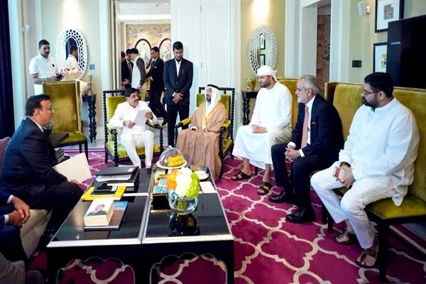 होटल के कमरे में पीली सोफों पर बैठे अतिथि, मुख्यमंत्री कागज़ पढ़ रहे हैं, गुलाबी कालीन
